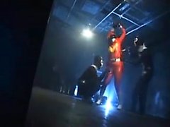 Sexy Superheld in orange Latex aufgereiht und gefoltert b